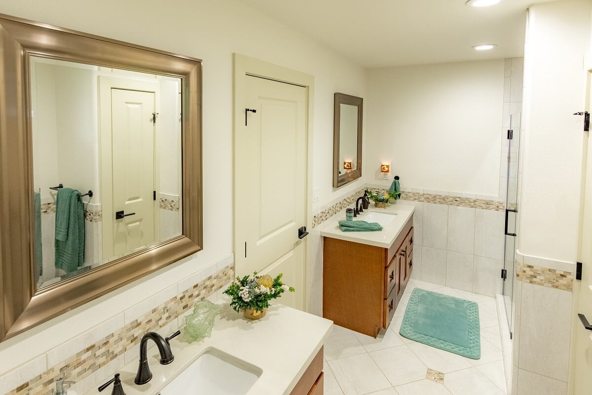 A well-lit, spacious bathroom featuring two sinks with mirrors, tiled walls, wooden cabinets, and decorative plants.