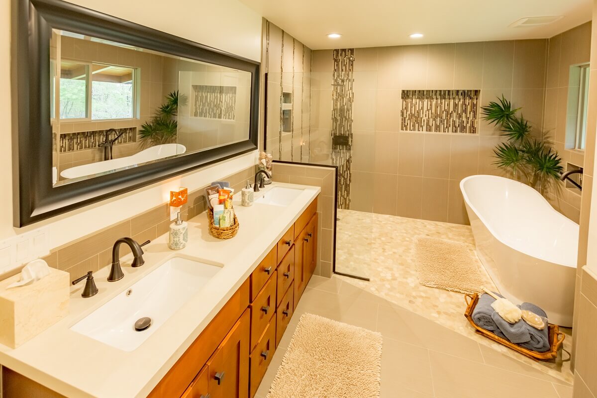 A modern bathroom featuring a double vanity with mirrors, a large bathtub, tiled walls, and a window overlooking greenery.