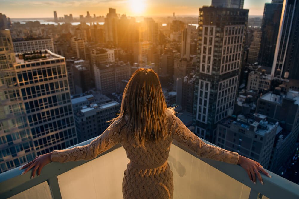 A woman looks over her balcony in NYC, overjoyed at returning from the Exclusive Hawaii Rehab